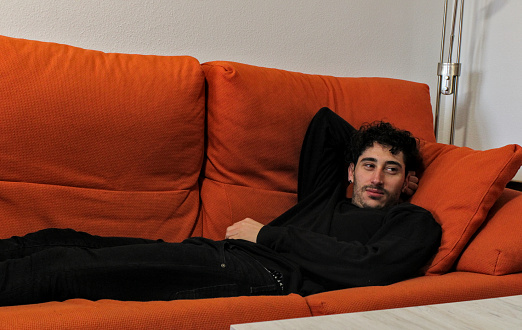 Single young white guy lying on sofa at home, curly hair, resting happy