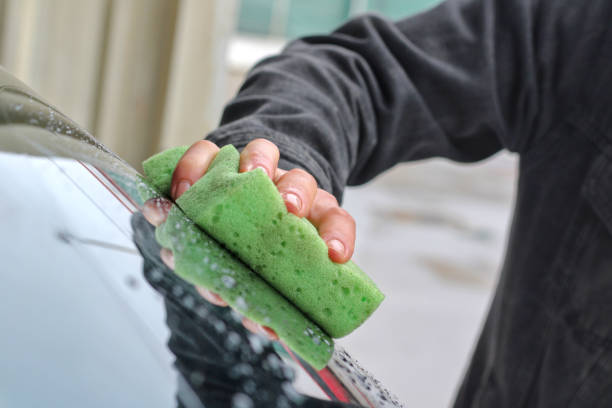 Young white man washing car windows with sponge, sponge in foreground