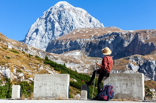 Woman Tourist Sitting on a Concrete Road Block, Admiring the Beauty of Mount Mangart in Autumn Colors