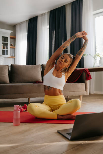 istock Confident young sporty woman doing stretching exercises while training at home with laptop of foreground 1879721432
