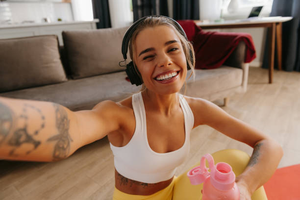Happy sporty woman making selfie while resting on exercise mat after home workout