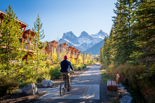 People riding a bicycle on walking trail in residential area. Town of Canmore street view in fall season. Alberta, Canada.