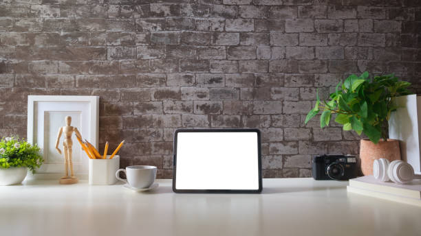 istock Modern workspace with a tablet computer, pot plant, notebook and coffee cup on white desk. Blank screen monitor for graphic display montage. 1879748217
