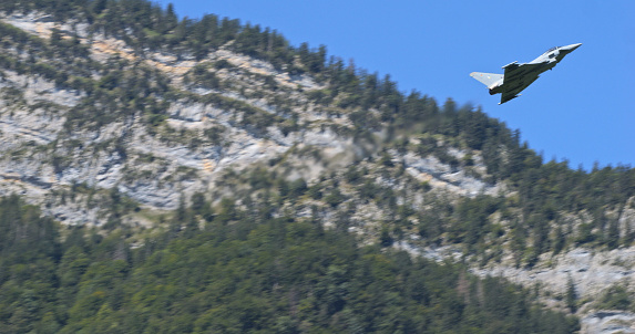 Mollis, Switzerland, August 19, 2023: A stealth fighter jet cruises above an alpine forest, its silhouette