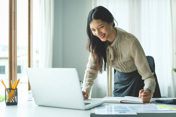 istock Young asian female office worker sitting in bright office and working on computer laptop. 1879800632