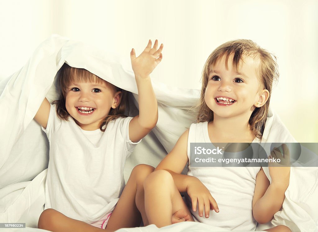 happy little girls twins sister in bed under the blanket happy little girls twins sister in bed under the blanket having fun, smiling Baby - Human Age Stock Photo