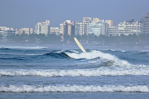 Sea near the beach, waves with white foam. City buildings in background.