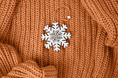 Wooden snowflake toy for a Christmas tree on a knitted wool sweater. Festive background. Peach Fuzz Color of Year 2024