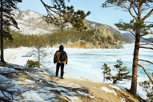 A male traveler admires the beautiful view of the frozen Lake Baikal. Winter travel, hiking, outdoor activities.