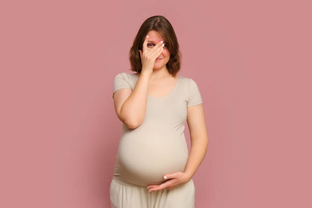 a shy pregnant woman on a pink studio background. pregnancy of a shame woman with a belly - women guilt uncomfortable human face imagens e fotografias de stock