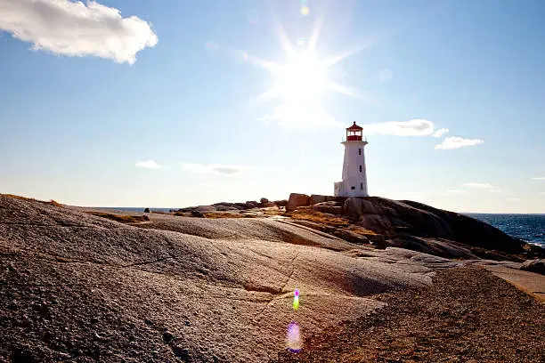 On a beautiful summers day, the setting sun moves past the light house guarding Peggy's Cove.