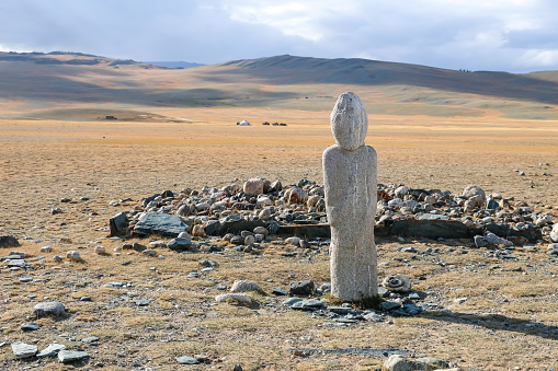 Balbal statue, marking a burial site, dating back 2,000 years in the Kazakh Bayan-Olgii Province of the Altai Mountains of Western Mongolia. The Turkic warrior human image carvings, made from a single stone, stand out in remote areas of the mountains marking the graves of warrior ancestors. A nomadic herder ger camp can be seen in the background.