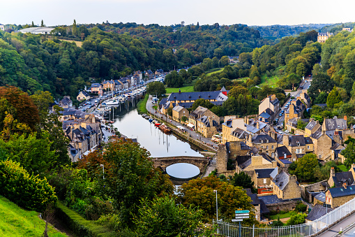 In this captivating photograph, the historic river port of Dinan unfolds in a timeless tableau of medieval charm and riverside allure. The stone buildings along the waterfront, bearing centuries of history, create a picturesque scene against the backdrop of the flowing river.

The aged architecture, characterized by half-timbered houses and charming facades, reflects in the tranquil waters below, creating a stunning reflection of Dinan's timeless beauty. Quaint cafes and shops line the quays, inviting visitors to savor the atmosphere while enjoying views of boats gently bobbing in the harbor.

The cobbled streets leading down to the riverbank contribute to the medieval ambiance, offering a nostalgic journey through the heart of Dinan's maritime past. The towering clock tower, a sentinel of the town's history, stands proudly overlooking the scene, adding a vertical dimension to the panoramic view.

As sunlight bathes the port in a warm glow, shadows dance on the stones, highlighting the textures of the historic buildings. This image encapsulates the essence of Dinan's river port—a place where history, architecture, and the gentle flow of the river converge, inviting all to step into a scene of enduring beauty and cultural richness.