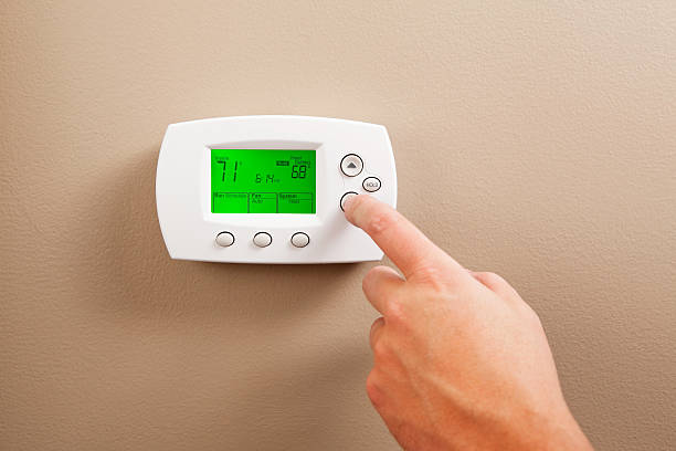 Hand Turning Down Digital Programmable Thermostat As a energy saving measure a male hand is turning down a digital programmable thermostat. The temperature reads 71 degrees, the adjusted temperature on the right is 68. Turning a furnace down while away or at night reduces electricity and gas consumption. thermostat photos stock pictures, royalty-free photos & images
