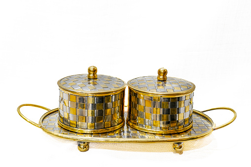 Decorated with an engraving of a gold and silver squares checked pattern. Placed on a small tray with feet and handles isolated in white background.