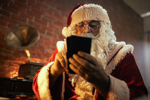 Santa Claus is talking on the phone in his office and writing in a book