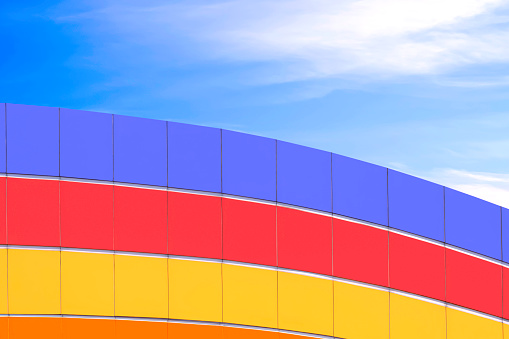 Geometric pattern background of colorful curve aluminium composite tiles wall decoration on high section outside of modern building against blue sky