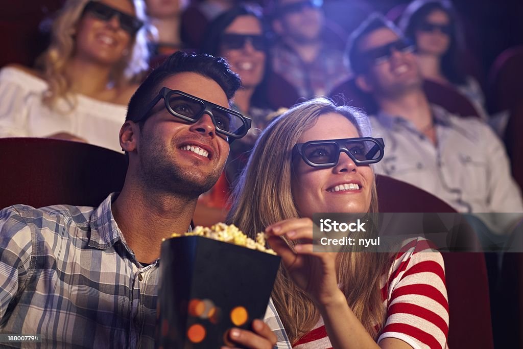 Happy couple in 3D movie Happy couple sitting in movie theater, watching 3D movie, eating popcorn, smiling.. Movie Theater Stock Photo