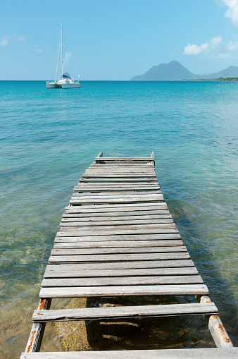 Old wooden pier and catamaran moored in tropical bay of Martinique, with Le Diamant and Le Morne Larcher mountain in background (Anse Mabouya, Sainte Luce, Martinique)