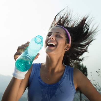 A young and confident female runner of Indian ethnicity splashing water on her body to cool herself while running in hot summer and giving toothy smile.