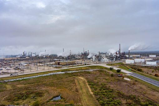 Aerial view of a Fuel Refinery in Port Arthur Texas with fuel storage, pipelines, steam rising from tall chimneys and an overcast sky above.