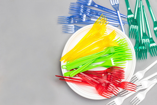 Bright colourful plastic tableware. Plastic  forks, straws on plate. Paper colored glasses. Reuse, environmental concept. Flat lay. Grey background