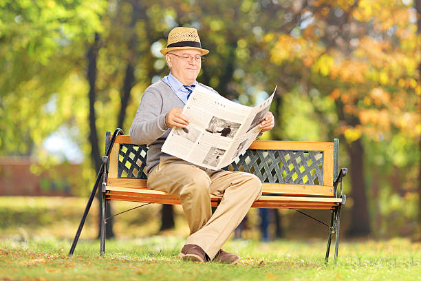istock Senior gentleman seated on bench reading a newspaper 188023126