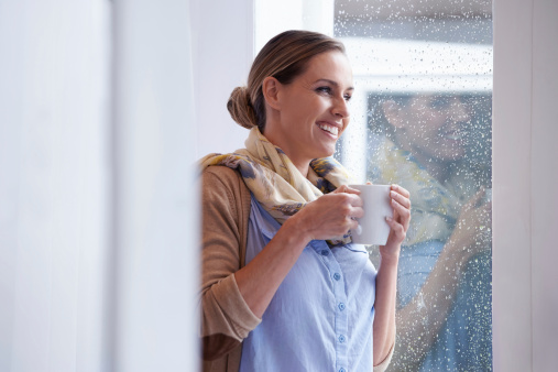 An attractive young woman standing by the window and drinking coffee