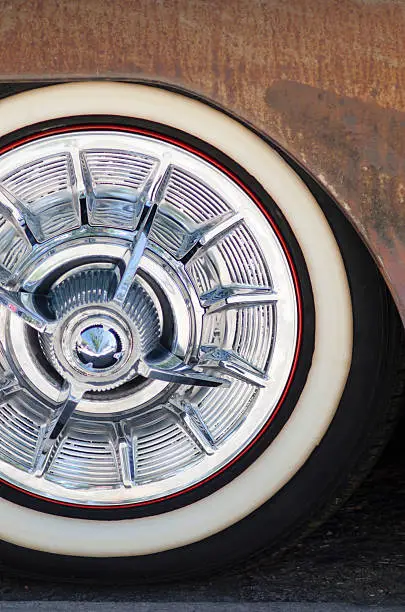The shiny chrome hubcap of a 1950 Pontiac Silver Streak is in sharp contrast to the rusted body of the vehicle.