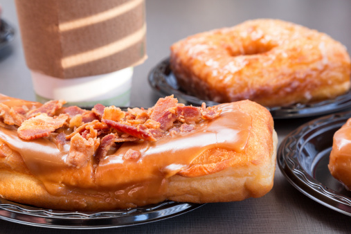 Maple donut with bacon on top, other donuts and coffee in the background