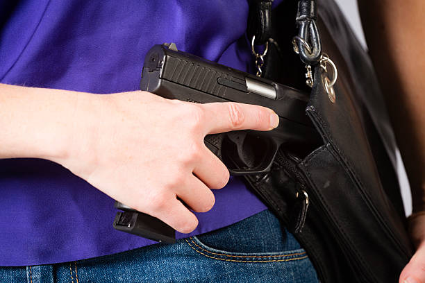 Woman Carrying Handgun A close-up of a woman holding a handgun in a purse. wallet gun stock pictures, royalty-free photos & images