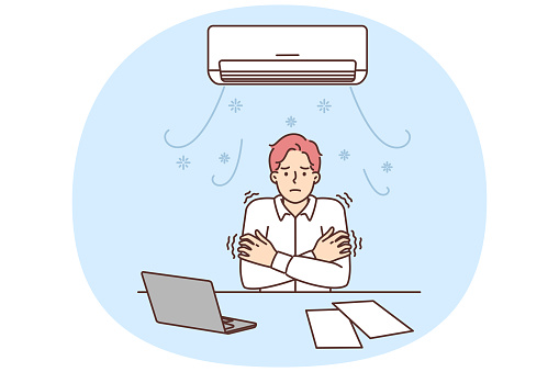 Man sitting at office desk under air conditioner freezes due to cold temperatures or broken climate equipment. Guy tries to warm up after being cold during working day