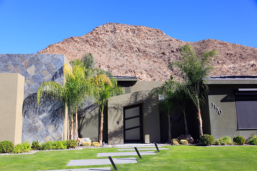 Palm Springs, California, United States- Modern stone and concrete home. Rocky desert  hill as background. Palm Trees in front of home.