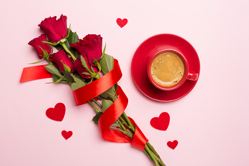 Red cup of coffee with roses on color background, top view