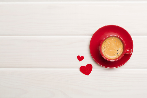 Red cup of coffee with hearts on wooden background, top view
