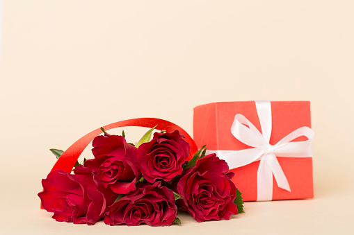 Sophisticated woman's gift arrangement: top view luxe roses, fashionable box, heart figures, and confetti artfully placed on a ruby background, with a text or ad space