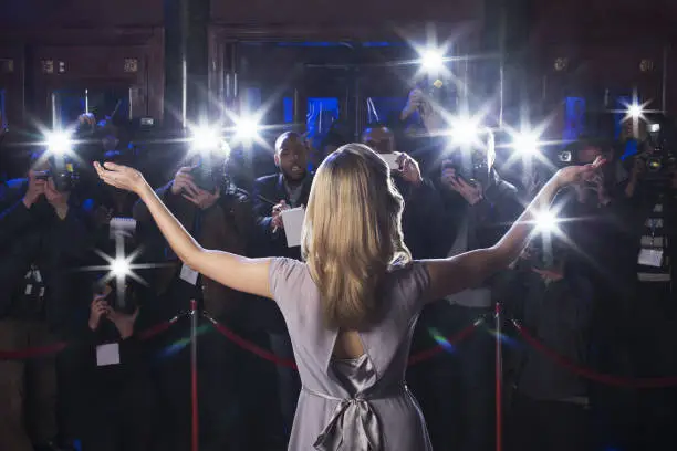 Photo of Rear view of female celebrity with arms outstretched to paparazzi at red carpet event