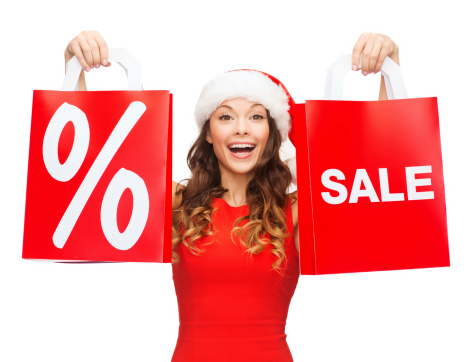 shopping, sale, gifts, christmas, x-mas concept - smiling woman in red dress and santa helper hat with shopping bags