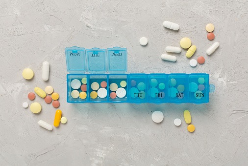 Daily pill organizer with medications on concrete background, top view
