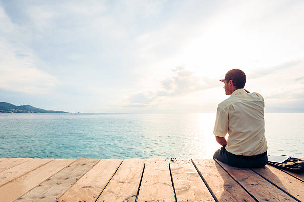 istock Business man sitting on pier looks out over water 188070320