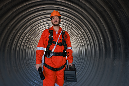 Portrait engineer or technician with safety uniform and safety harness work under a huge tube at the construction site.