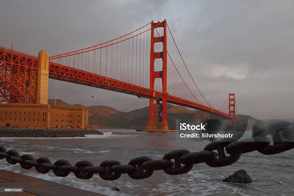 Golden Gate Bridge and Fort Point at sunrise. On an overcast morning, a break in the clouds allows a bit of warm light to wash over the Golden Gate Bridge and Marin Headlands. Architecture Stock Photo