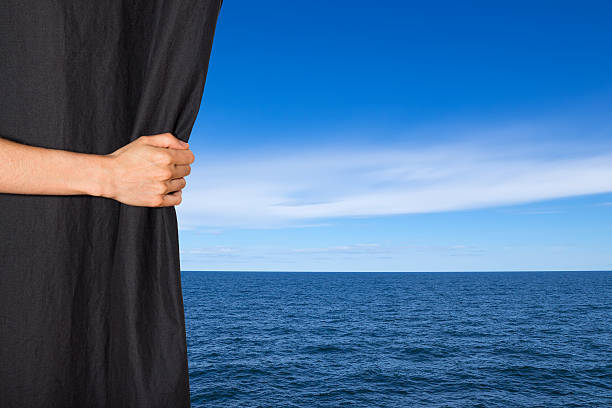 istock Hand opening black curtain with sea and sky behind it 188075738