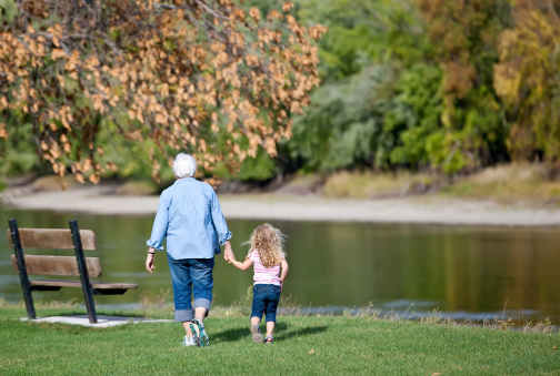 Young girl holding Grandma's hand as they walk to a park bench next to the (Mississippi) River.