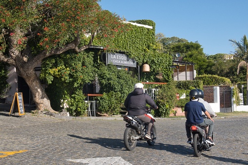 colonia del sacramento, uruguay - november 1 2022: people on motor cycles passing by a bar covered in ivy in the Barrio historica of the colonial UNESCO world heritage site