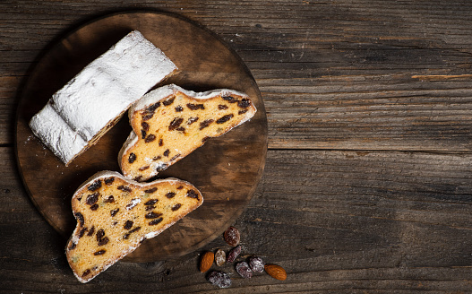 Christmas stollen - traditional German bread on a brown wooden table. Festive dessert made of dough, nuts and raisins, sprinkled with powdered sugar. Copy space