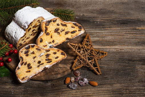 Christmas stollen - traditional German bread on a brown wooden table with Christmas decoration. Festive dessert made of dough, nuts and raisins, sprinkled with powdered sugar. From above, with copy space