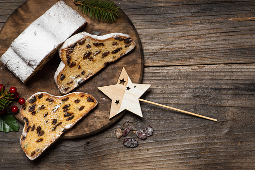 Christmas stollen - traditional German bread on a brown wooden table with Christmas decoration. Festive dessert made of dough, nuts and raisins, sprinkled with powdered sugar. From above, with copy space