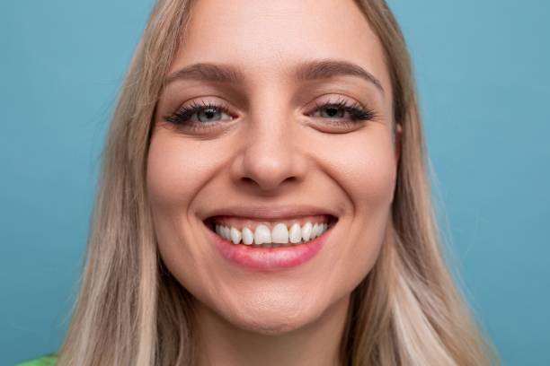portrait d’une jeune femme blonde joyeuse et en bonne santé avec un sourire hollywoodien sur fond bleu - mid adult women human skin neat good condition photos et images de collection