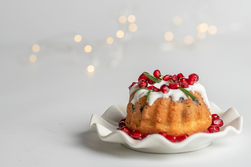 Christmas mini bundt cake sprinkled with sugar and fruit, served in a plate. With Christmas decoration on a white background